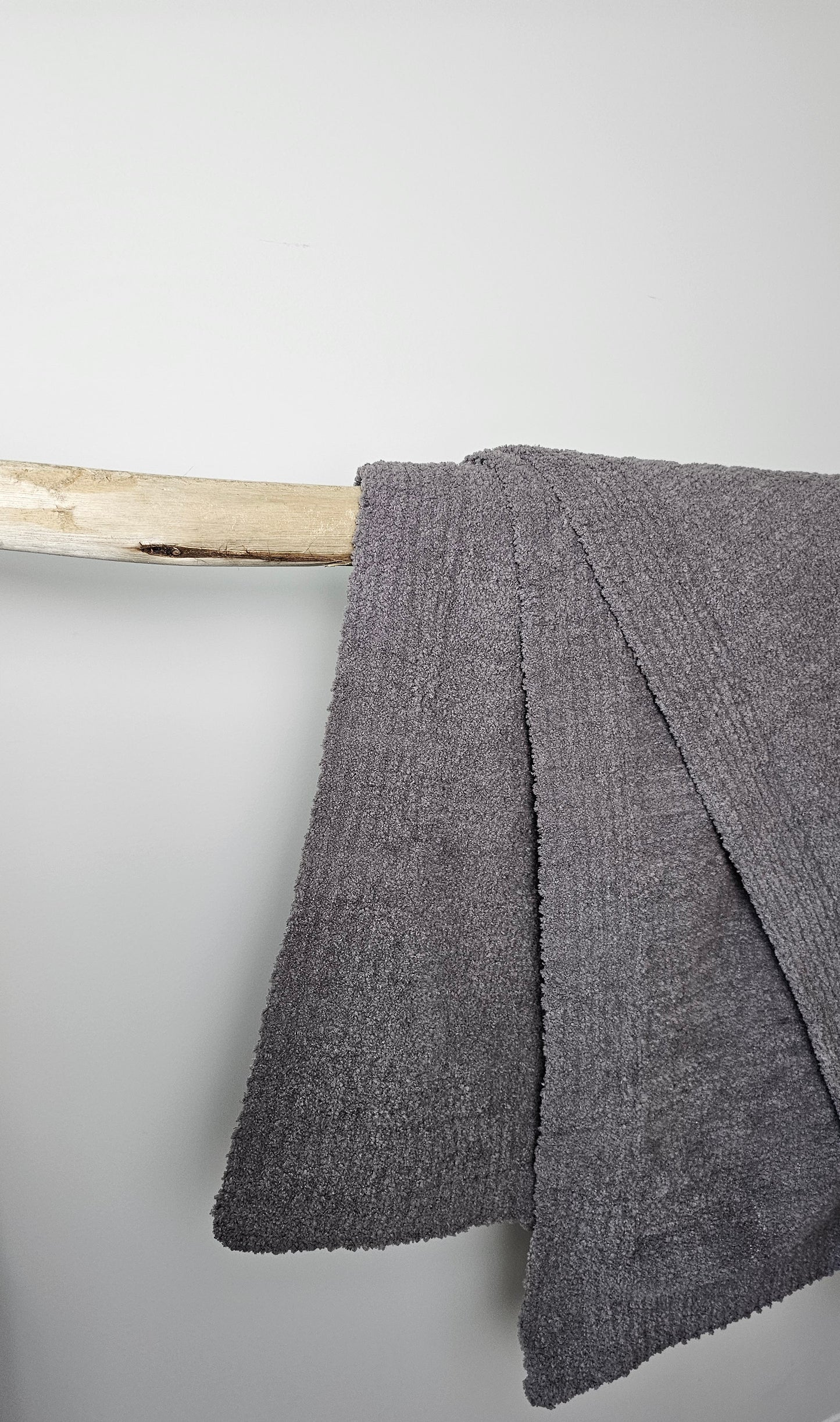 Charcoal Nest throw blanket hanging on driftwood, showcasing its rich color and cozy double-layer design