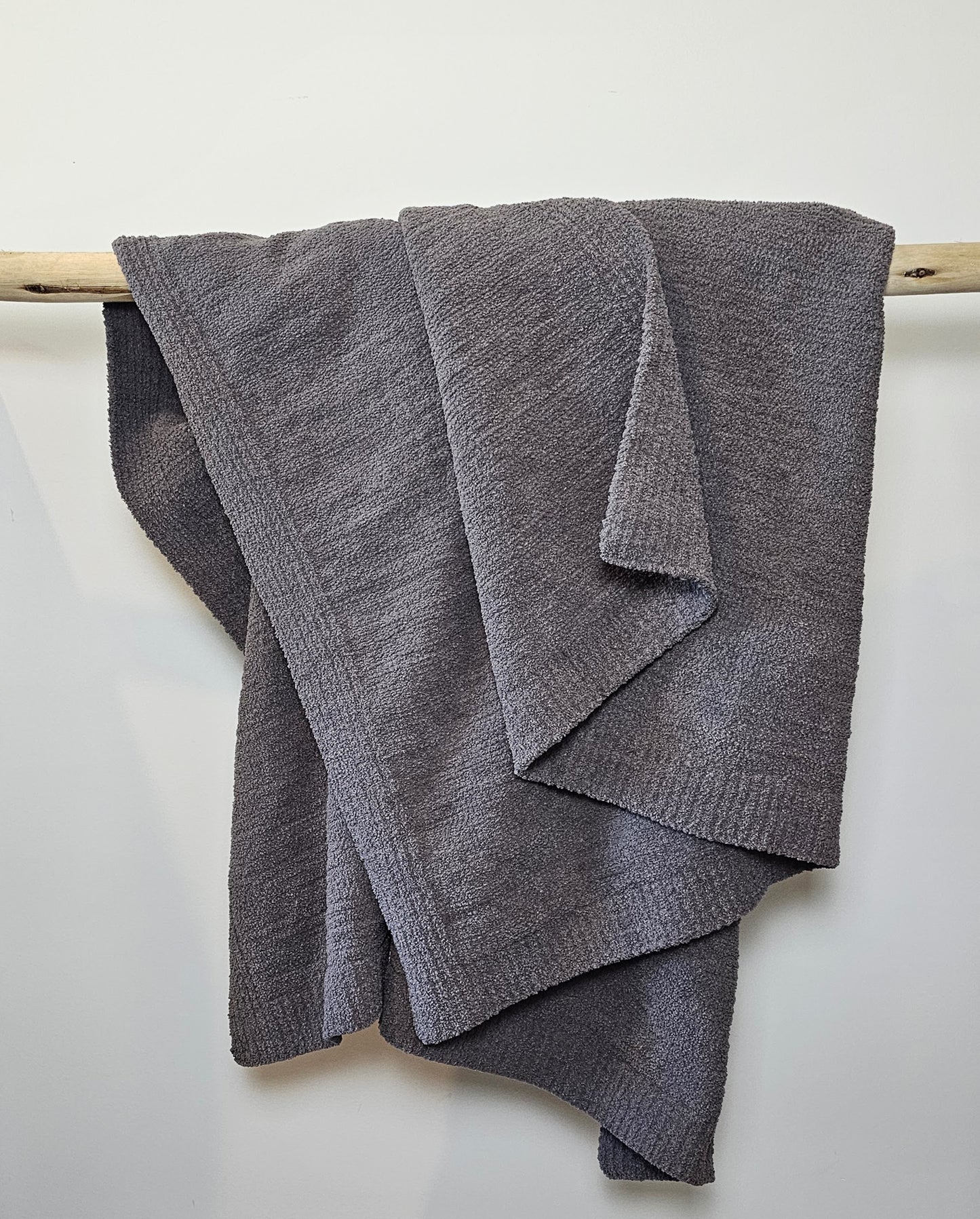 Deep Charcoal Nest throw blanket draped over driftwood, highlighting its plush texture and bold, modern tone.