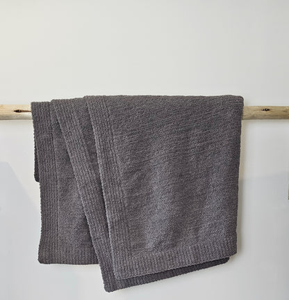 Charcoal Nest throw blanket draped over driftwood, showcasing its deep, rich color and ultra-soft texture.