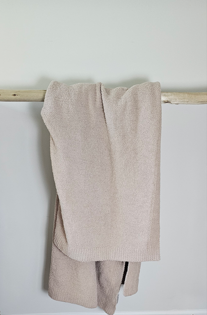 Muted Fossil Greige Nest throw blanket, elegantly displayed over driftwood, blending softness and natural tones highlighting its high quality soft fabric