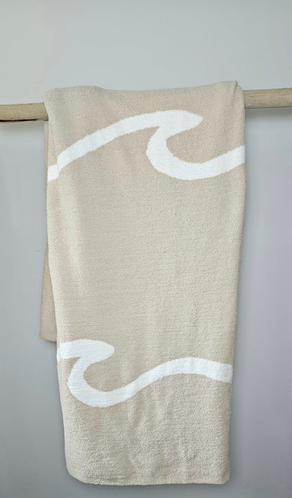 Wave nest throw blanket artfully draped over driftwood, featuring its ocean-inspired design. Soft and stylish Wave throw hanging on driftwood, embodying beachside comfort and elegance. showcasing its Double sided design with sand beige and white

