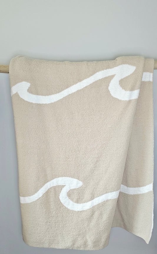 Wave nest throw blanket artfully draped over driftwood, featuring its ocean-inspired design. Soft and stylish Wave throw hanging on driftwood, embodying beachside comfort and elegance. showcasing its Double sided design with sand beige and white

