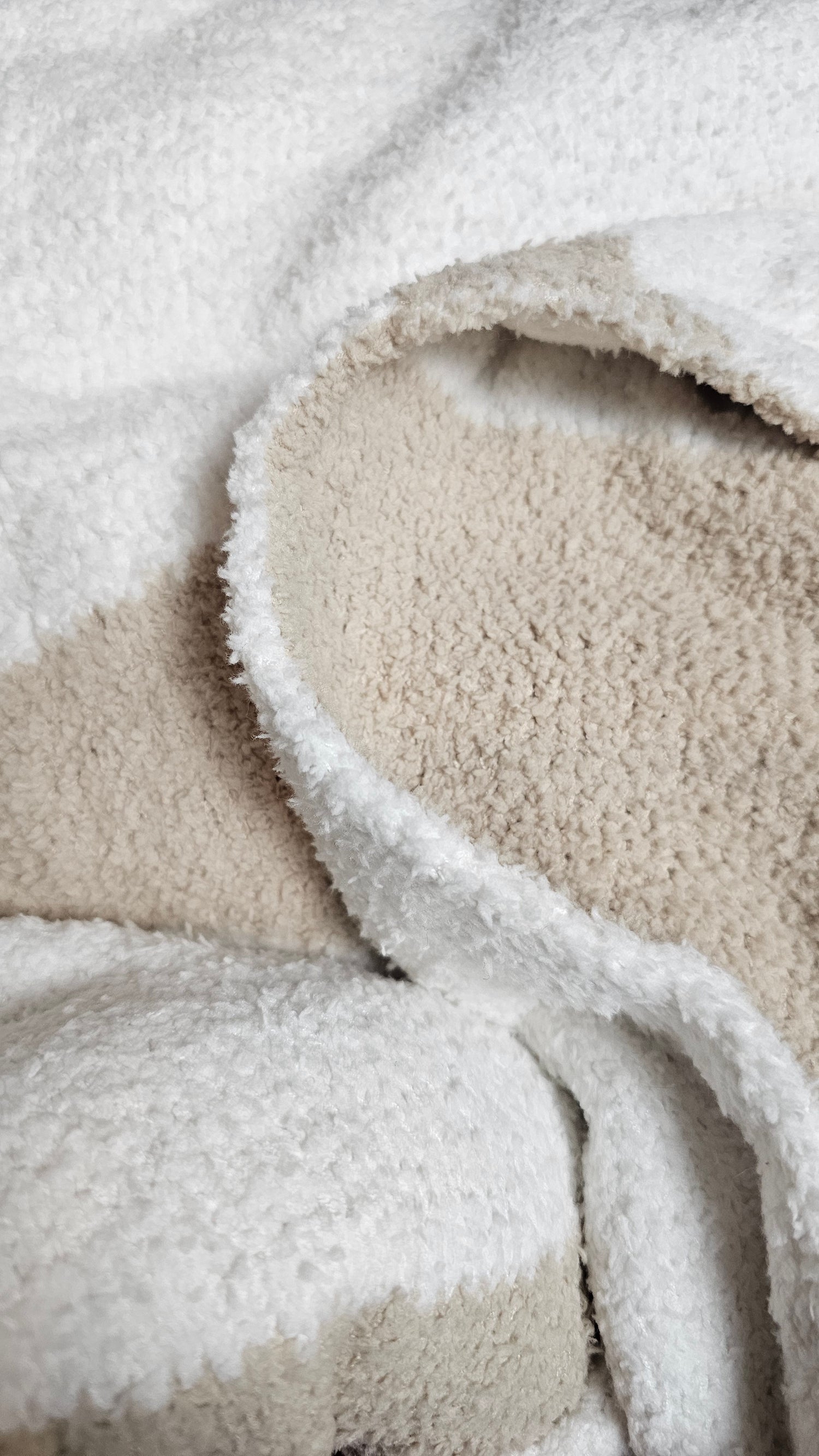 Wave nest throw blanket close up to show the plush and durable fabric, featuring its ocean-inspired design. Soft and stylish Wave throw hanging on driftwood, embodying beachside comfort and elegance. showcasing its Double sided design with sand beige and white

